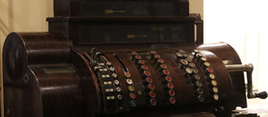 An antique wooden cash register, with many multicolored buttons and a crank for operating.